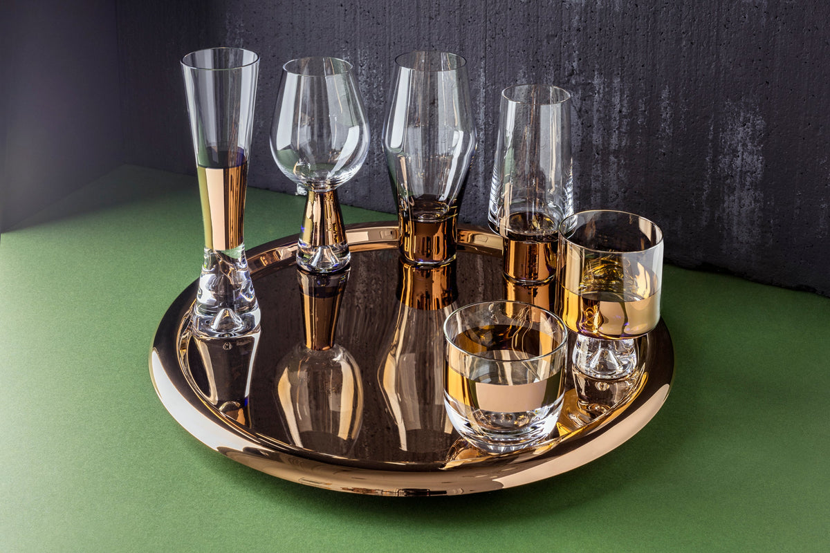 Tom Dixon Tank glasses, tumblers and decanter on a round copper tray against a dark wall