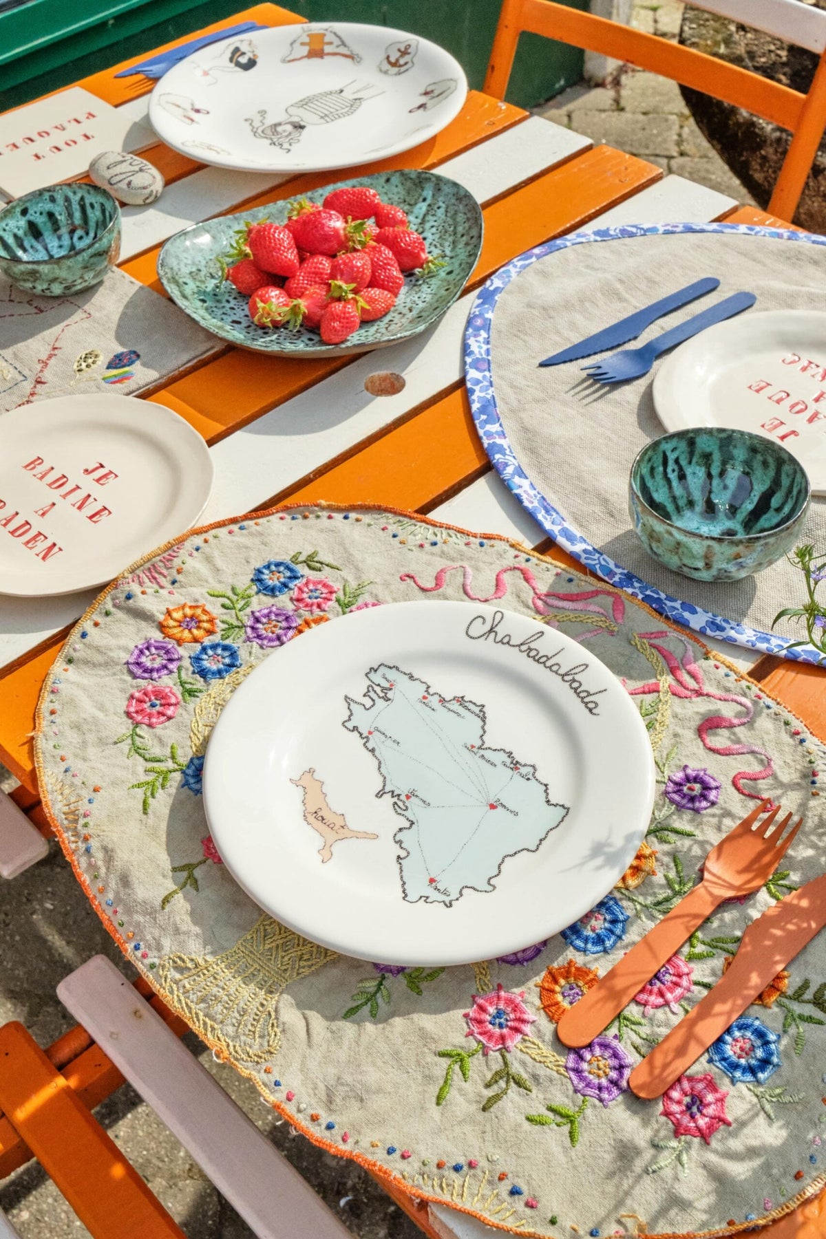 Gien x La Prestic Ouiston plates on an embroidered tablecloth with strawberries, on an orange garden table