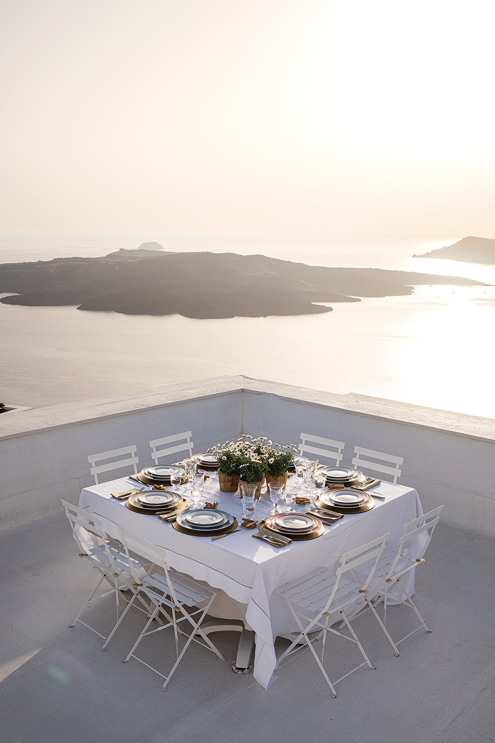 A table set with Victoria de Borbón's Santorini Collection on a terrace overlooking the Santorini caldera