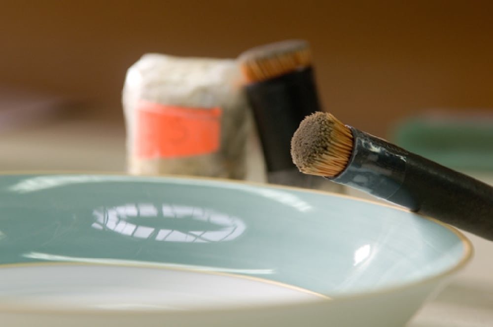 A brush dusting colour onto a pale celadon porcelain bowl in the Seignolles workshop
