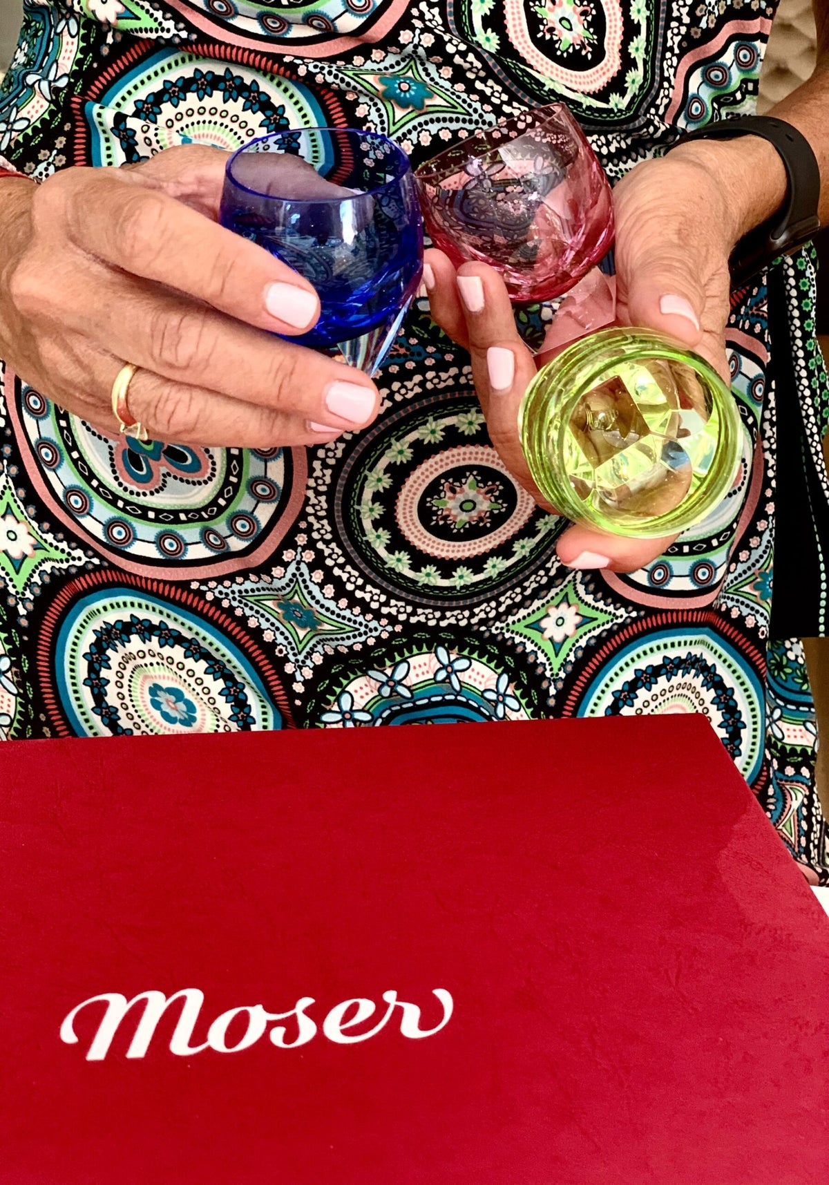 Hands holding coloured Moser crystal glasses above a red Moser box
