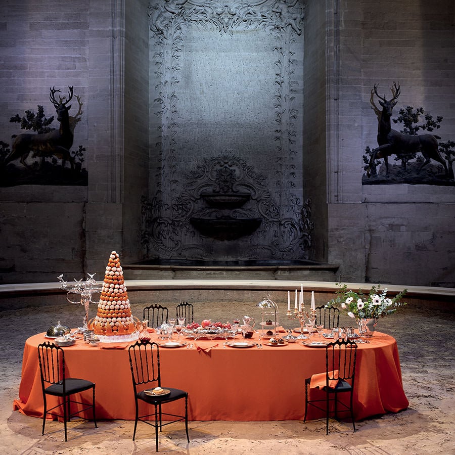 A banquet table dressed with Ercuis silverware and a tall pièce montée in a stone hall
