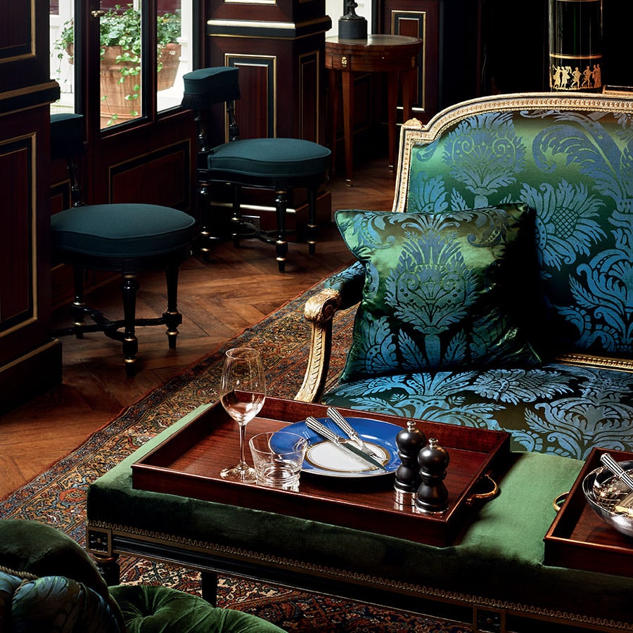 A tray with Ercuis cutlery, a plate and a wine glass on a green velvet ottoman in a classic interior