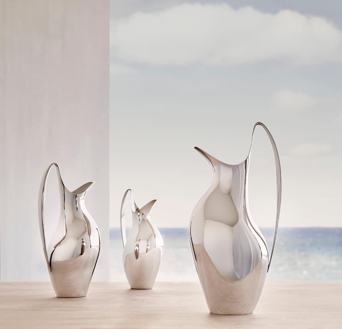 Three sculptural Georg Jensen stainless steel pitchers against the sea