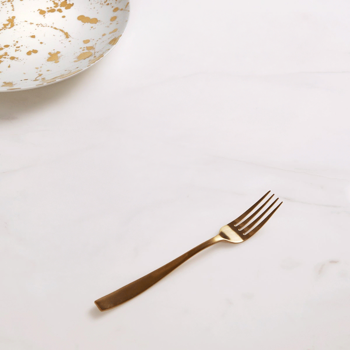 Gold Jonathan Adler fork beside a white and gold bowl