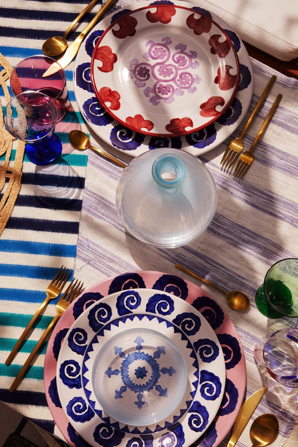 Overhead view of Emporio Sirenuse hand-painted ceramic plates in red, pink and blue on a striped tablecloth