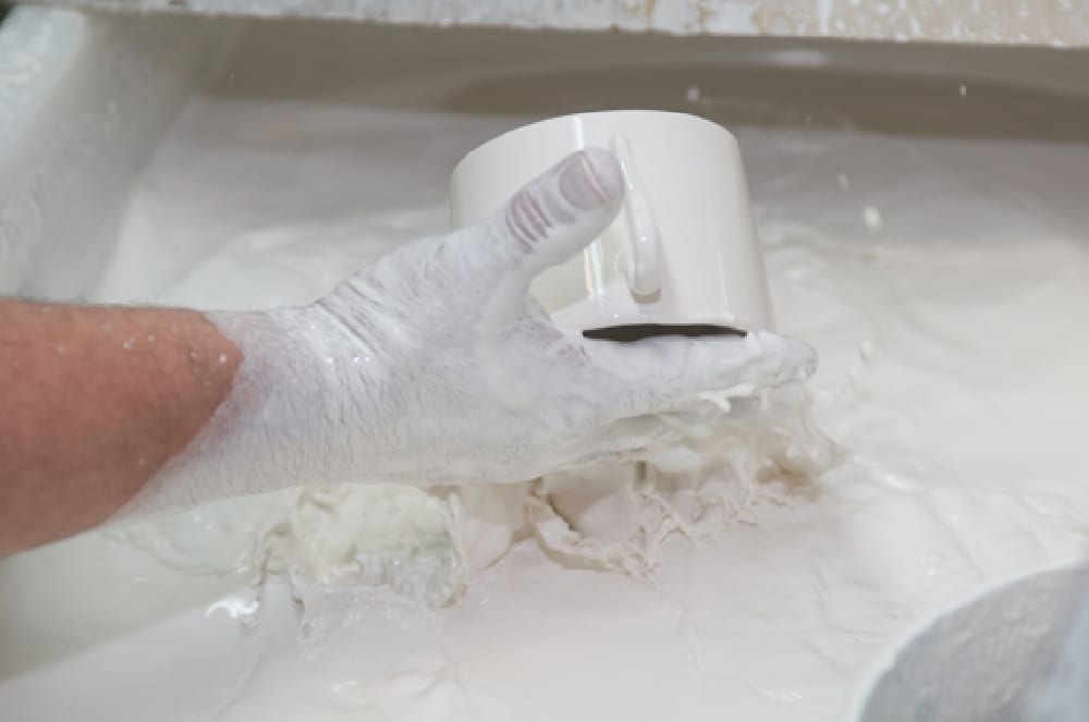 A gloved hand dipping a Seignolles porcelain cup into white glaze