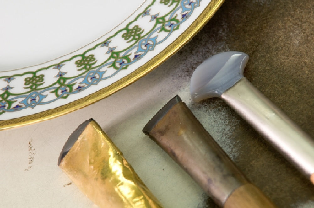 Gilding tools beside a Seignolles plate with a green and gold patterned rim