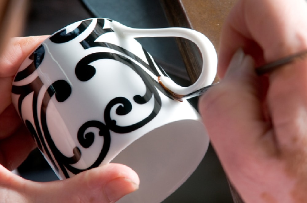 An artisan painting black scroll decoration on a Seignolles porcelain cup