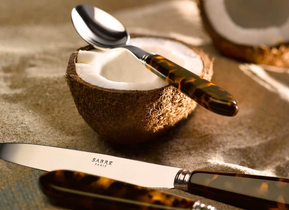 Sabre knife and spoon with tortoiseshell-effect handles beside a coconut