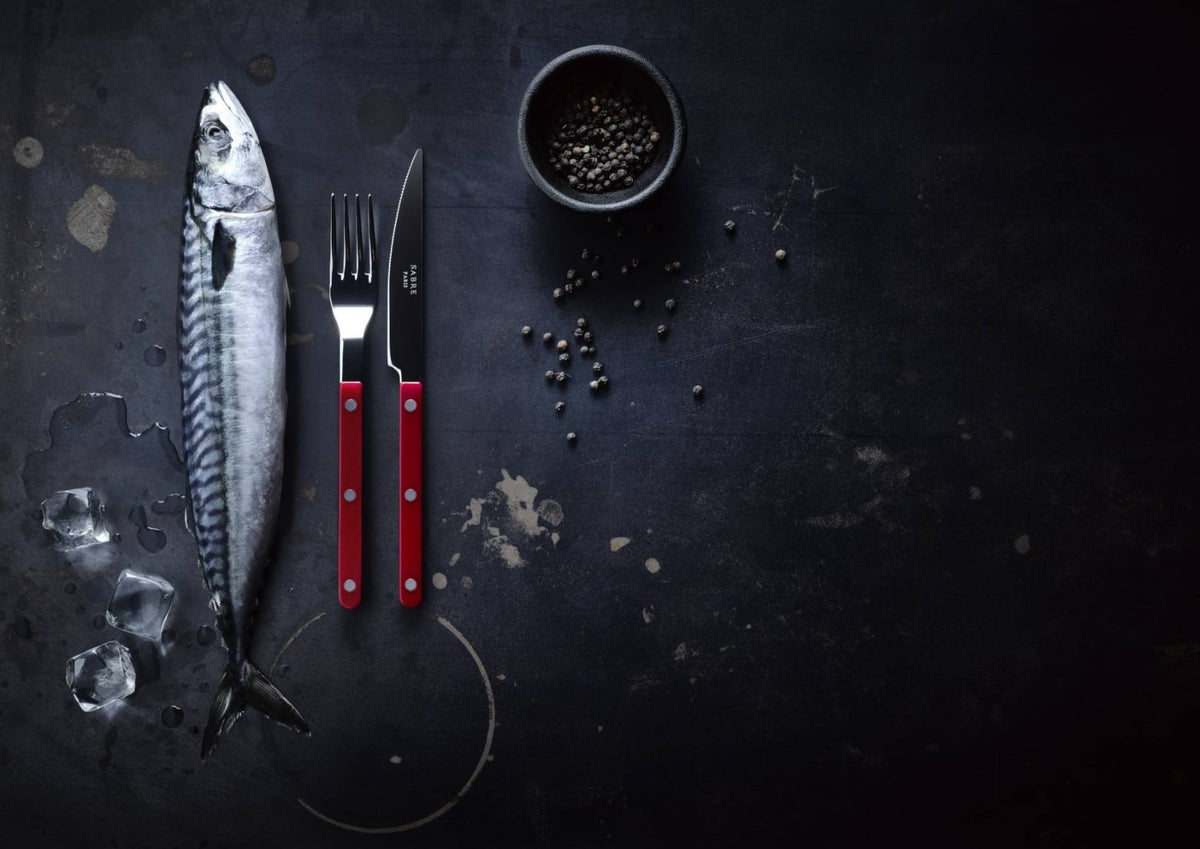 Sabre knife and fork with red handles beside a mackerel
