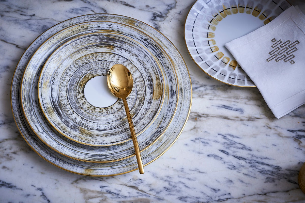 Stacked Marie Daâge plates with gold-painted decor and a gold spoon
