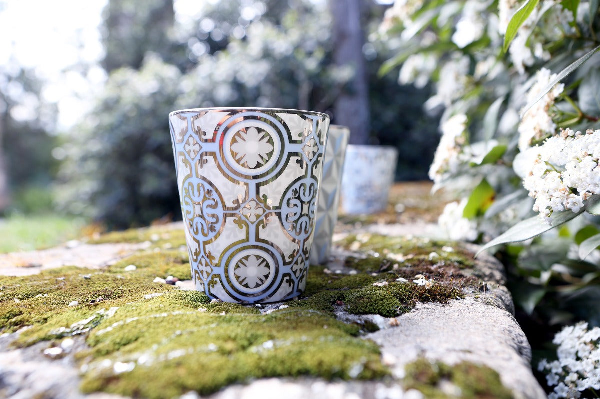 Rose et Marius scented candle in a blue and white patterned glass on a mossy stone wall